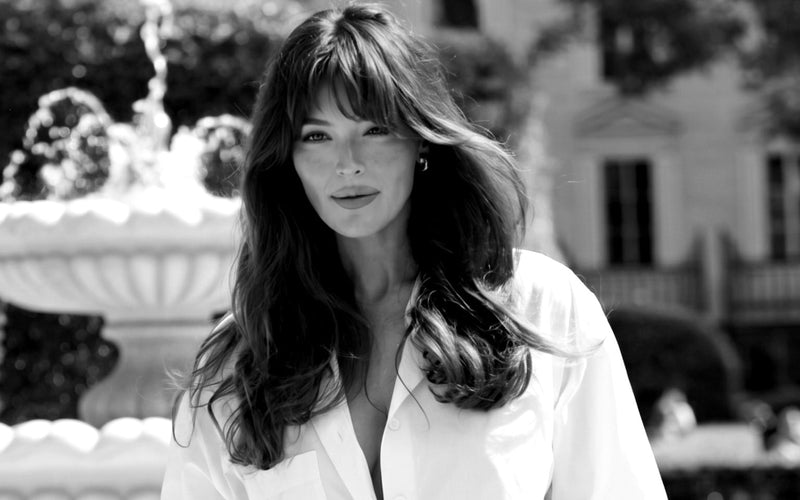 Black and white portrait of a woman in a white shirt and Faza Atelier high waisted trousers beside a fountain